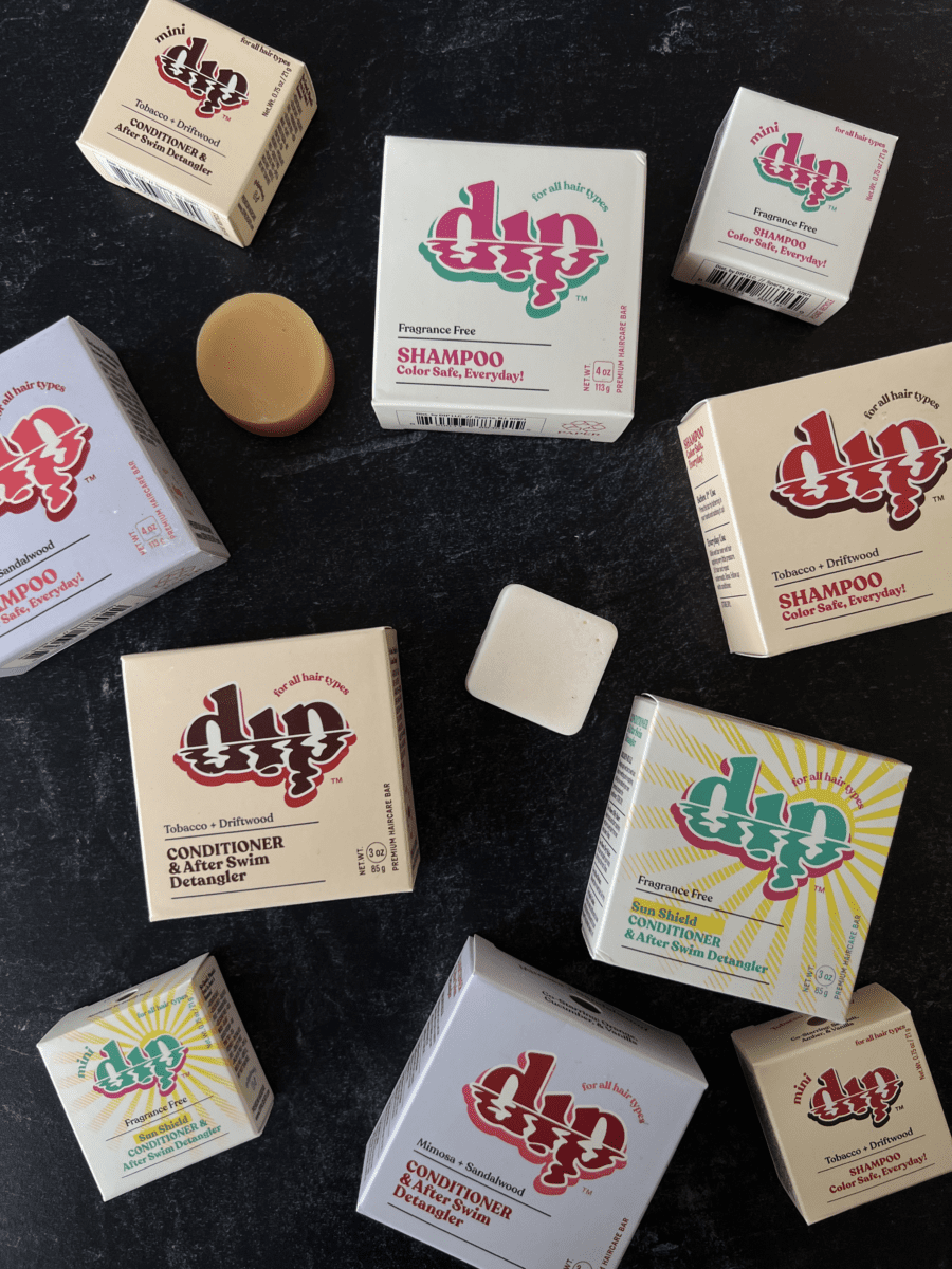 Colorful shampoo and conditioner bars in their box packaging arranged on a black background. One mini shampoo bar and one mini conditioner bar are unwrapped among the boxes.